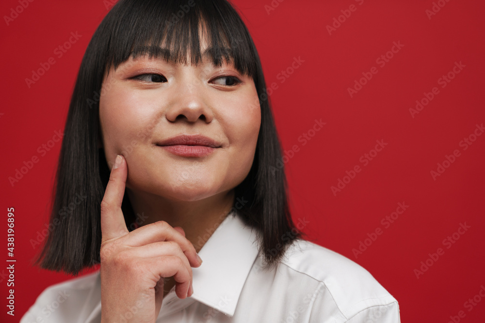 Young asian woman pointing finger at her cheek and looking aside Young asian woman pointing finger at her cheek and looking aside