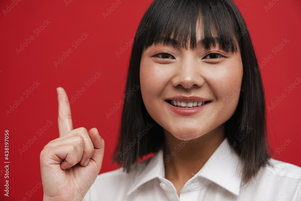 Young asian woman wearing shirt smiling and pointing finger upward Young asian woman wearing shirt smiling and pointing finger upward