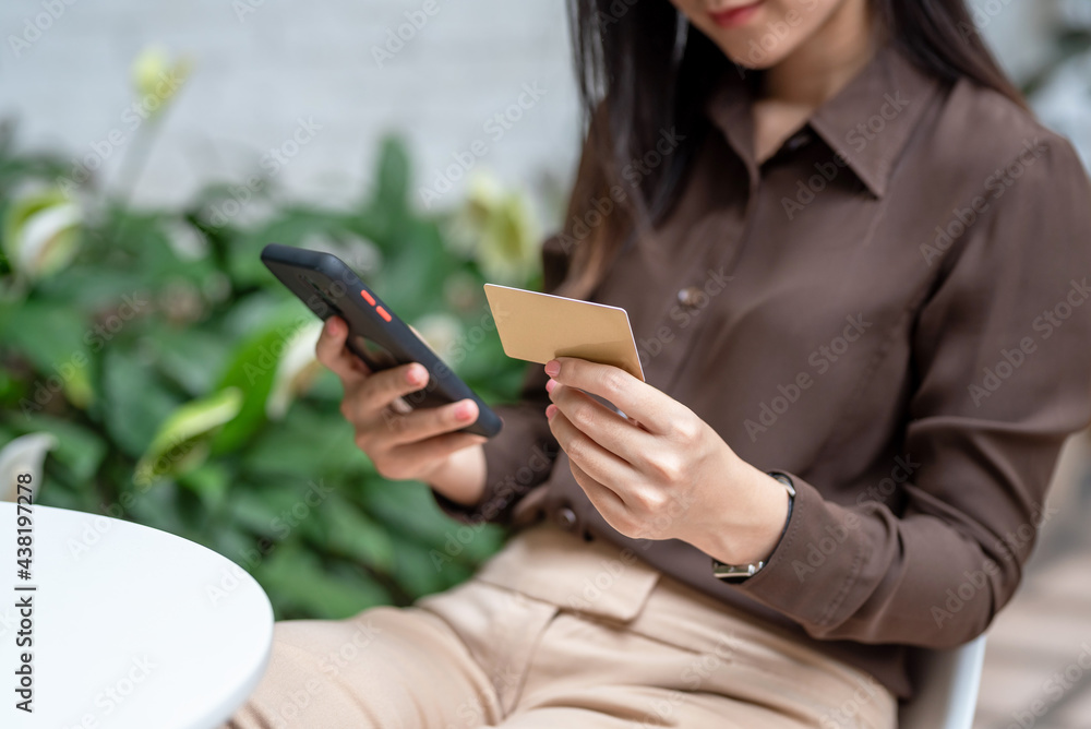 Close-up of a woman hand holding a credit card with a smartphone sitting chair in a café. Close-up of a woman hand holding a credit card with a smartphone sitting chair in a café.