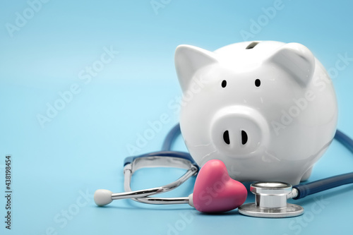 Piggy bank with stethoscope and heart isolated on light blue background with copy space. Health care financial checkup or saving for medical insurance costs concept.