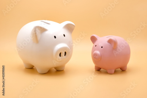 Front view of white and pink piggy bank for money saving isolated on pastel orange background.