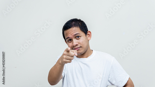 Confident and smile face expression of young Asian Malay man in white t-shirt pointing finger at the camera and people in front on isolated white background. Choosing you concept.