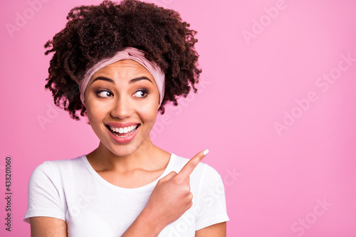 Photo of brunette optimistic lady point empty space wear white t-shirt hairband isolated on pastel pink background