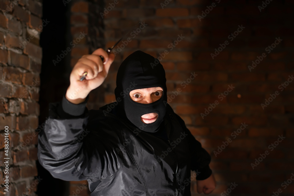 a bandit, terrorist, criminal in a black mask attacks with a knife in his hand in a dark room of an abandoned brick building