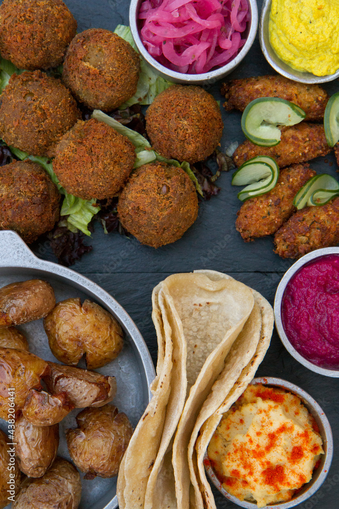 Vegan cuisine. Closeup view of fried potatoes, vegan fried kibbehs, lentil falafels, onion pickles, garbanzo, beets and carrot hummus, and corn tortillas on the table. Vegan cuisine. Closeup view of fried potatoes, vegan fried kibbehs, lentil falafels, onion pickles, garbanzo, beets and carrot hummus, and corn tortillas on the table.