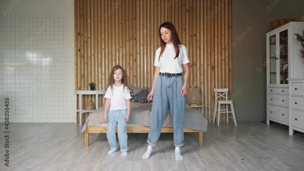 Brunette mother in white t-shirt and blue denim jeans teaches little daughter new dancing moves standing in large bedroom with stylish furniture Brunette mother in white t-shirt and blue denim jeans teaches little daughter new dancing moves standing in large bedroom with stylish furniture