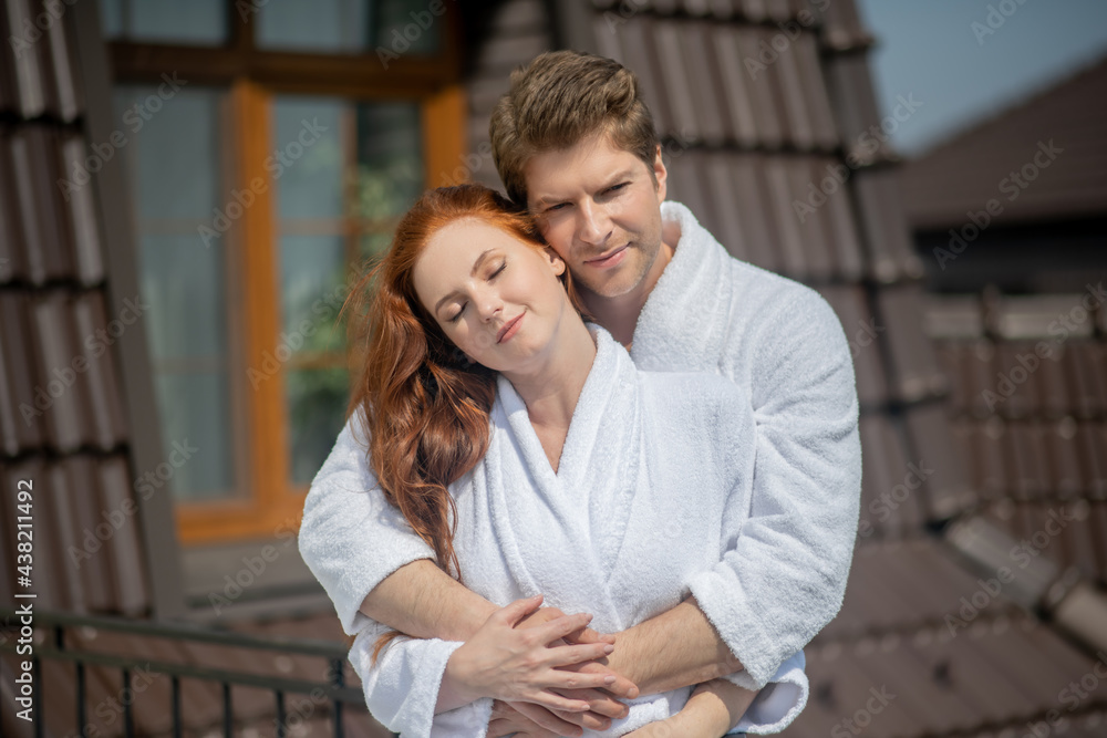 A couple in white bathrobes hugging and looking pleased and happy