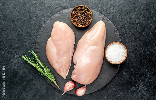 Raw chicken breasts with spices on a stone background