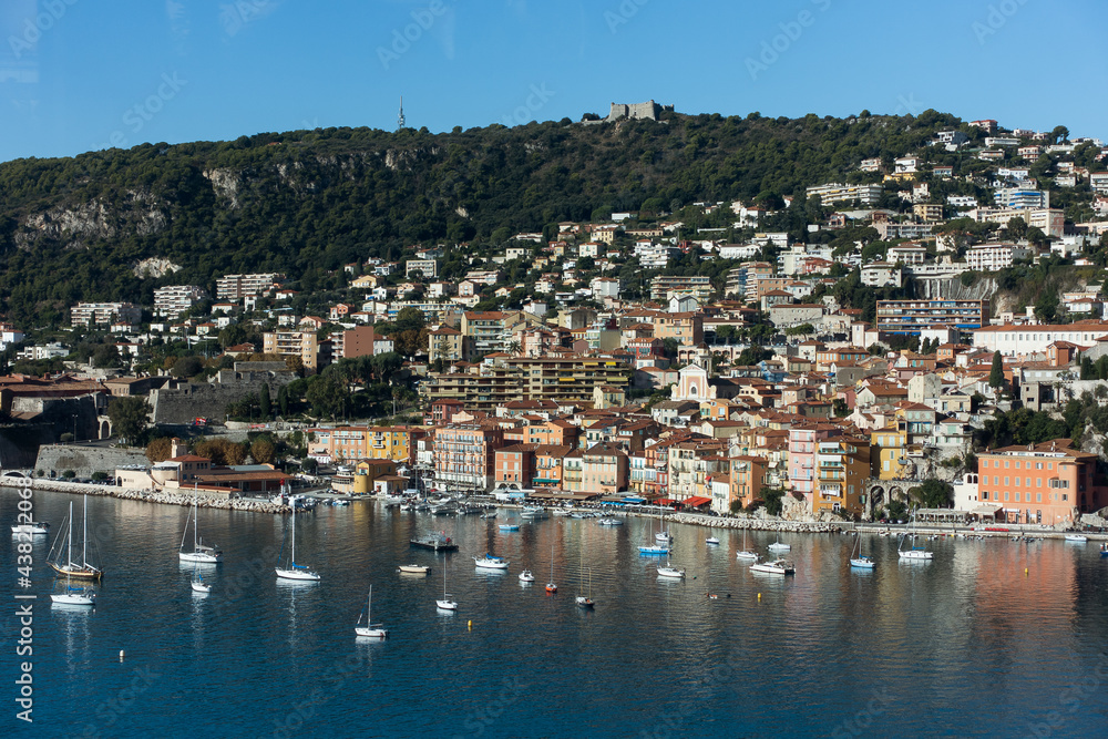 Blue sea with small luxury yachts and boats with cute village on a hill at background on sunny summer day. Aerial view of Mediterranean sea in french riviera. High quality photo