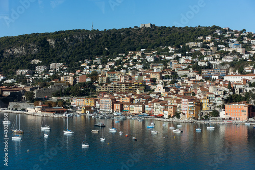 Fototapeta Naklejka Na Ścianę i Meble -  Blue sea with small luxury yachts and boats with cute village on a hill at background on sunny summer day. Aerial view of Mediterranean sea in french riviera. High quality photo