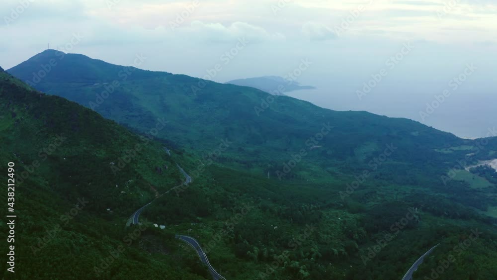 Aerial Panning Shot Of Winding Road On Mountain Near Sea Against Sky, Drone Flying Over Green Landscape At Dusk - Hue, Vietnam Aerial Panning Shot Of Winding Road On Mountain Near Sea Against Sky, Drone Flying Over Green Landscape At Dusk - Hue, Vietnam