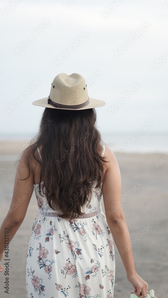 young girl walking on the beach at sunset with dress and hat