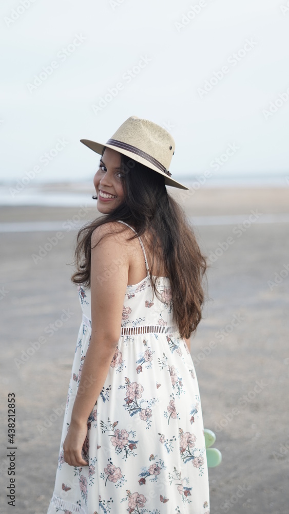 young girl walking on the beach at sunset with dress and hat