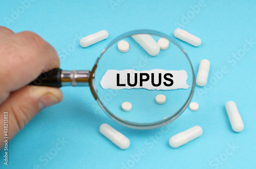 A man looks through a magnifying glass at pills and a leaf with the inscription - LUPUS