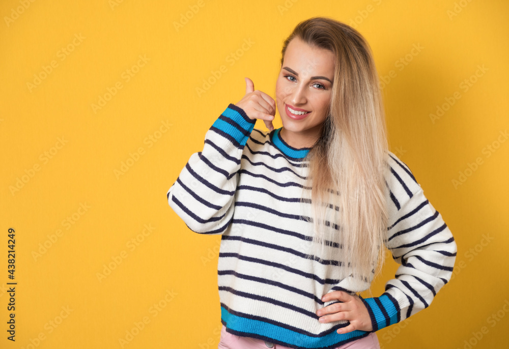 Call me, woman gesturing at speaking on phone while looking to camera, isolated on yellow background. Young woman on phone Call me, woman gesturing at speaking on phone while looking to camera, isolated on yellow background. Young woman on phone