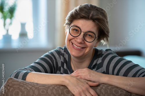 Smiling mature middle-aged woman sitting at home on the couch. Happy lady 50 years old, with glasses. 