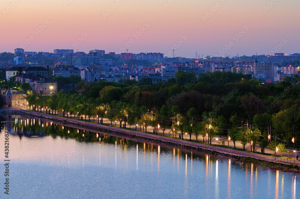 Ternopil, Ukraine-May, 11,2021:Picturesque morning landscape view of Ternopil. Empty motorway between city lake and park with green trees. Buildings in the background. Romantic and peaceful scene