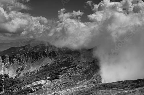 Immagine in bianco e nero di tratto di montagna immerso nelle nuvole.
