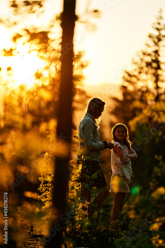 A girl in silhouette in sun set in the forest. Summer days. It is hot and warm. Two sisters are playing in the woods. Golden hour with strong and bright sunlight.