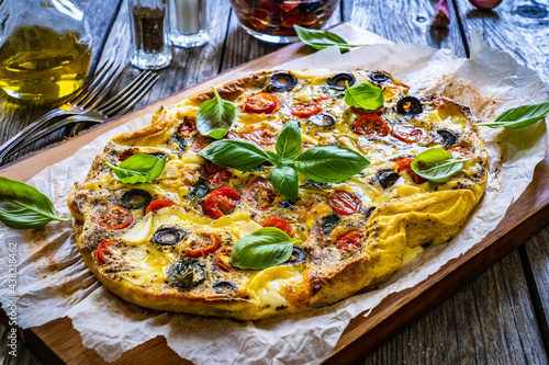 Frittata - scrambled eggs with mozzarella and vegetables on wooden table 