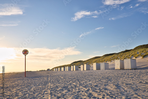 Horizontal view on a beach with a row of beach cabins at sunset in spring. North sea beach with dunes in Zeeland on a sunny day. Copy space.