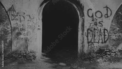 Black and white footage of dark gate with God is dead graffiti on the wall. photo