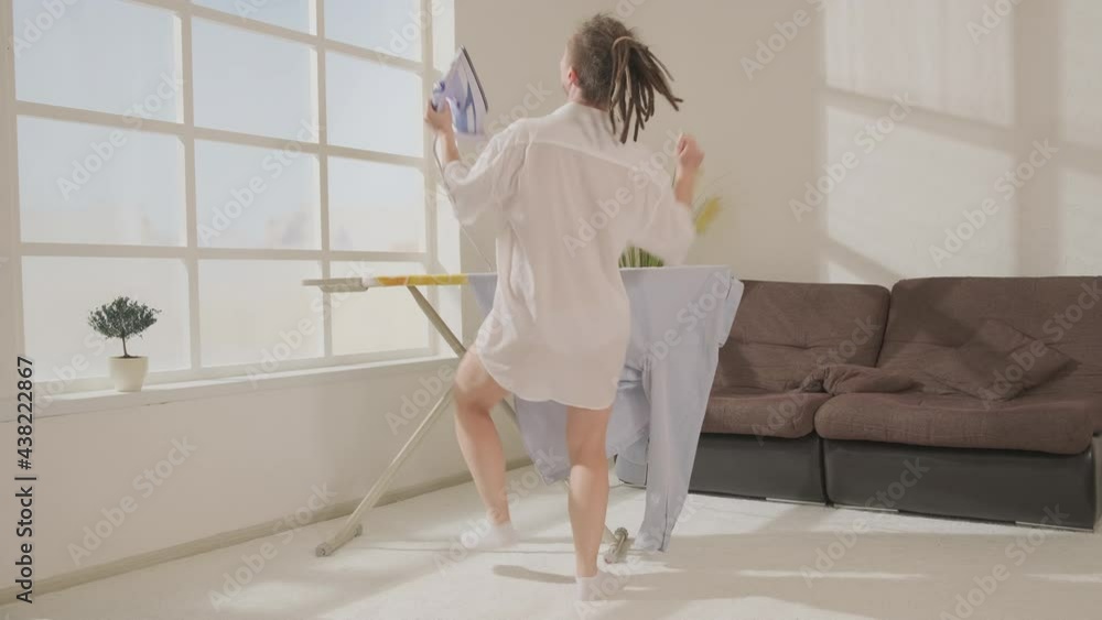 Dancing woman in man's shirt irons on ironing board, back view. Dancing woman in man's shirt irons on ironing board, back view.