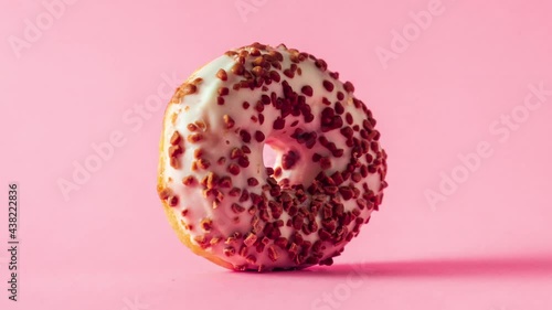 White chocolate donut with almonds topping rotating zooming in and out on pink background.