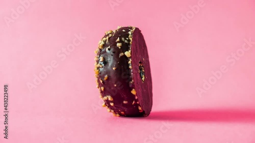 Chocolate donut with almonds topping rotating on pink background.