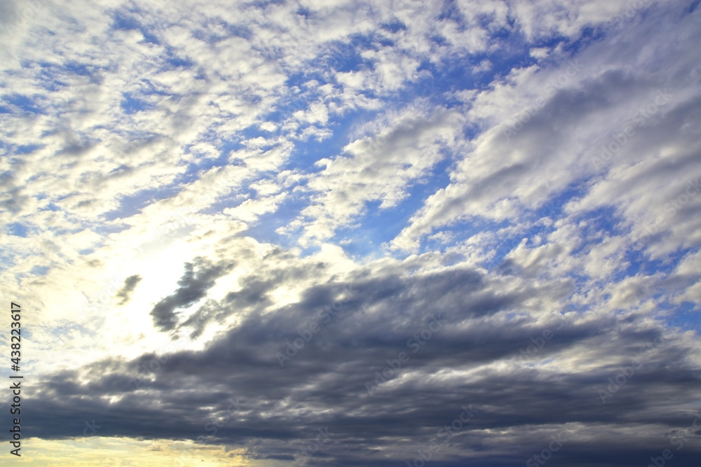 Obraz premium The bright sun hid behind light white clouds in the blue sky.