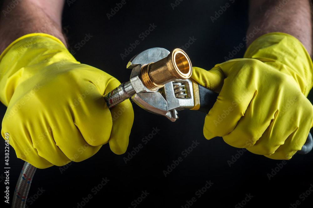 A plumber connects a high pressure hose when repairing equipment. Close-up of a hand of a master in gloves while working on a dark background A plumber connects a high pressure hose when repairing equipment. Close-up of a hand of a master in gloves while working on a dark background