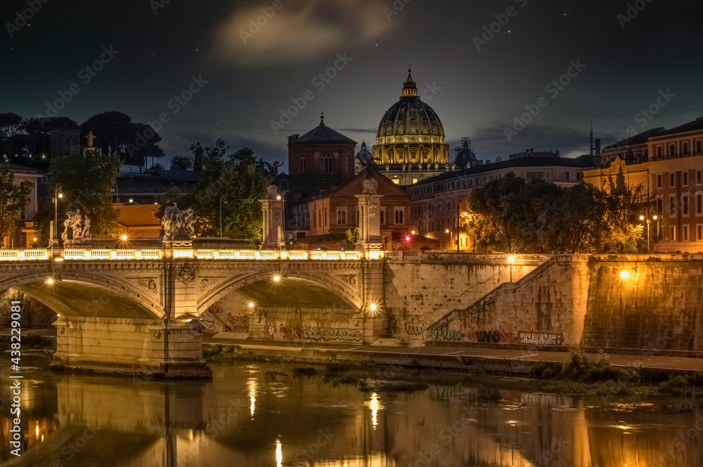 The Basilica of St. Peter in the Vatican is visible from the Eliev Bridge and the Tiber River. Night photo against the background of the starry sky. Rome, Italy