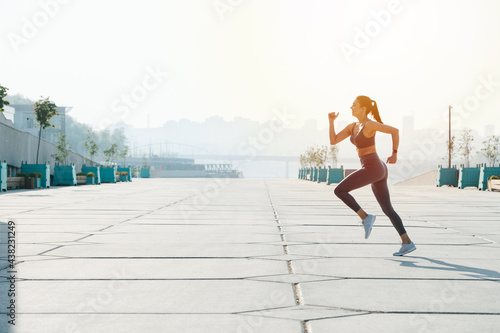 Sunlit brunette running on the pavement outdoors. Low angle