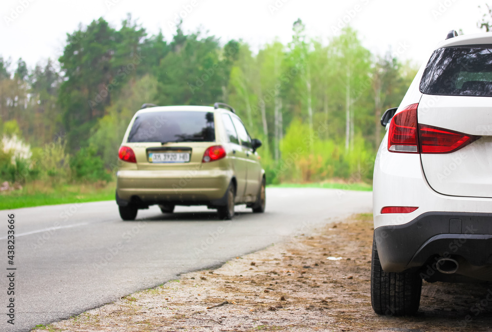 White SUV parked on the roadside in beautiful spring forest. An asphalt road among green trees on a spring day. Traveling by car through a native countryside. Amazing natural background.