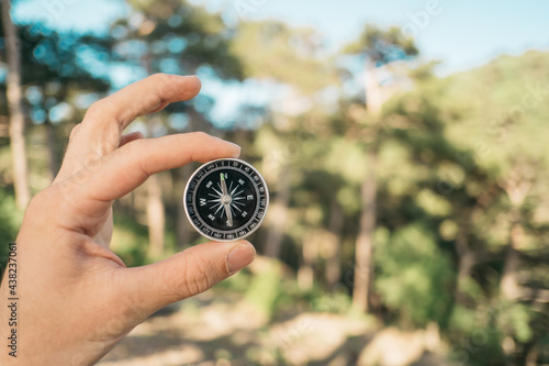 Man holds a compass in his hand in the forest on the background of trees.