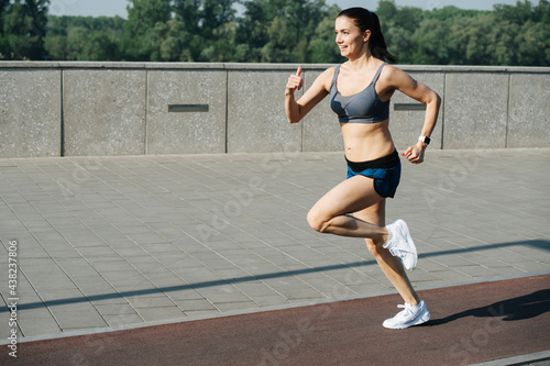 Exhilarated woman running fast outdoors on the track next to pavement sidewalk