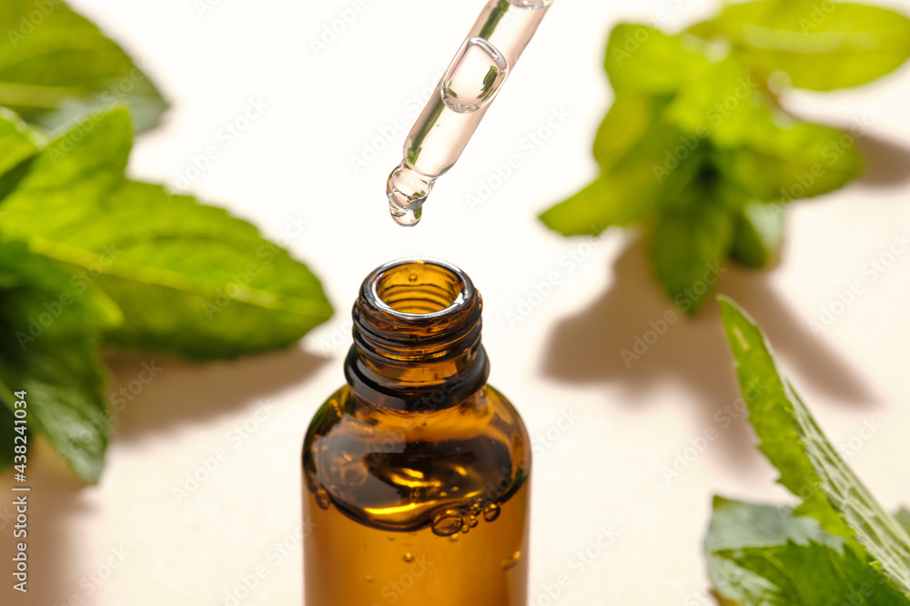Mint essential oil bottle on a beige background with mint leaves. Natural skin care cosmetics. Mint essential oil bottle on a beige background with mint leaves. Natural skin care cosmetics.