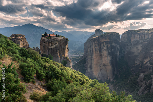 Scenic landscape of a wide mountain valley in Greece with bizarre cliffs, a dense forest at the foot of the mountains, and a small Christian monastery on top of a cliff