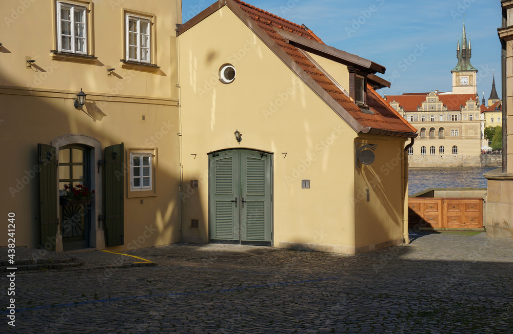 Small Square and passageway to the embankment of the Vltava River. Clock tower on the other side of the river. Prague, Czechia. - obrazy, fototapety, plakaty 