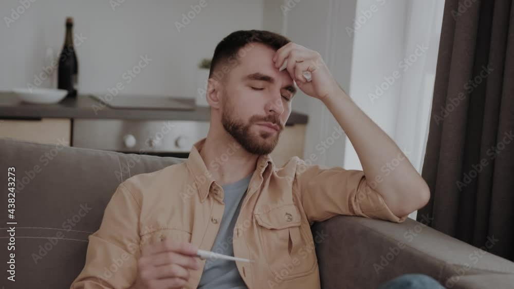 A young sick man measures the temperature with a thermometer. Fever and colds A young sick man measures the temperature with a thermometer. Fever and colds