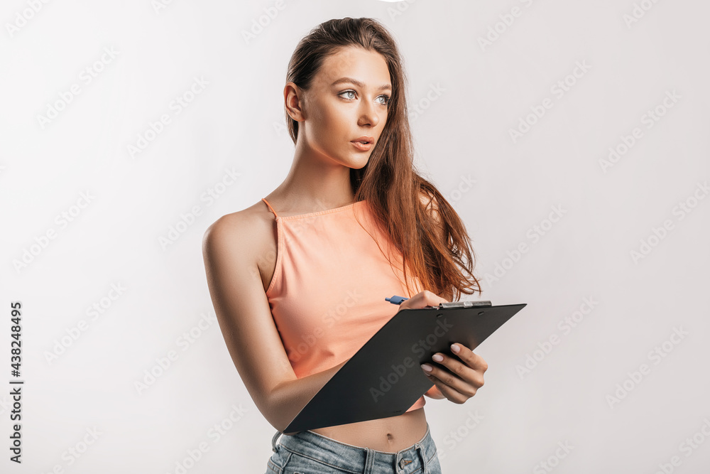Girl student writes information. Beautiful young business woman isolated on gray background. Achieving career wealth business concept. Mockup copy space. Hold a clipboard with documents Girl student writes information. Beautiful young business woman isolated on gray background. Achieving career wealth business concept. Mockup copy space. Hold a clipboard with documents