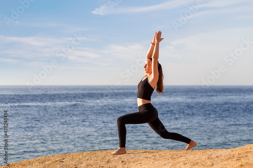 Young fitness woman practicing yoga at the seashore in the morning