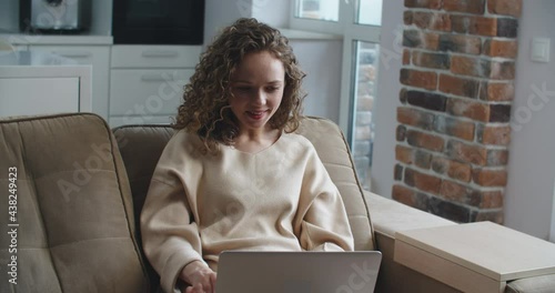 Happy woman with curly hair reads good news on laptop. Victory, winning. Call a friend to share the news. High quality 4k footage photo
