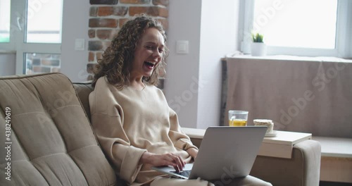 Happy woman with curly hair reads good news on laptop. Victory, winning. . High quality 4k footage photo