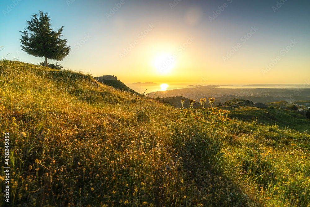 Orange sunset over the Sea of adriatic, with flower-covered hill slope in the foreground, and the Albanian city - Vlora
