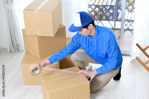 作業服を着た男性が引っ越しの段ボールを梱包するイメージ
 photo