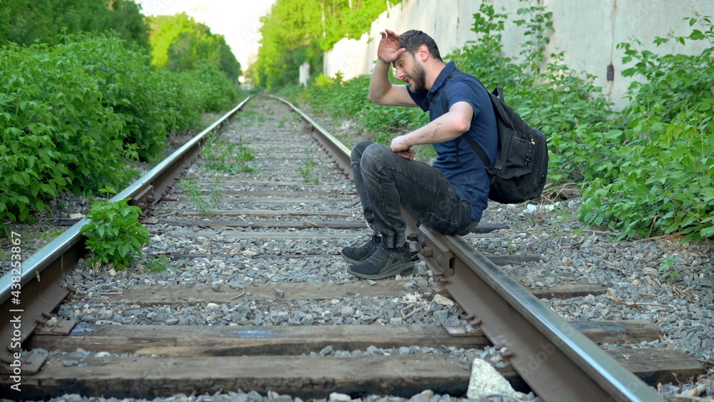 A man with a backpack on his back sat down to rest on the rails. Travel on railroad tracks. Old train track A man with a backpack on his back sat down to rest on the rails. Travel on railroad tracks. Old train track