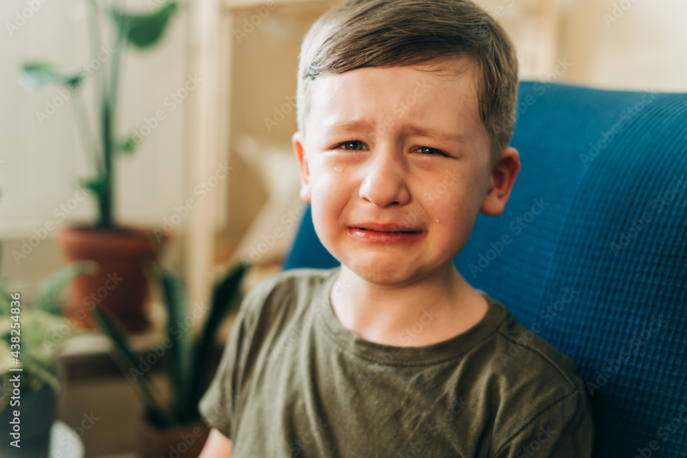 Close up portrait of crying little kid boy, sitting on couch indoors at home. Upset child Close up portrait of crying little kid boy, sitting on couch indoors at home. Upset child