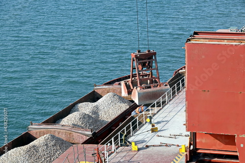 Loading bulk cargo of limestone from barges into a bulk carrier by using ship cranes and grabs at the port of Campha, Vietnam. October,2020. 