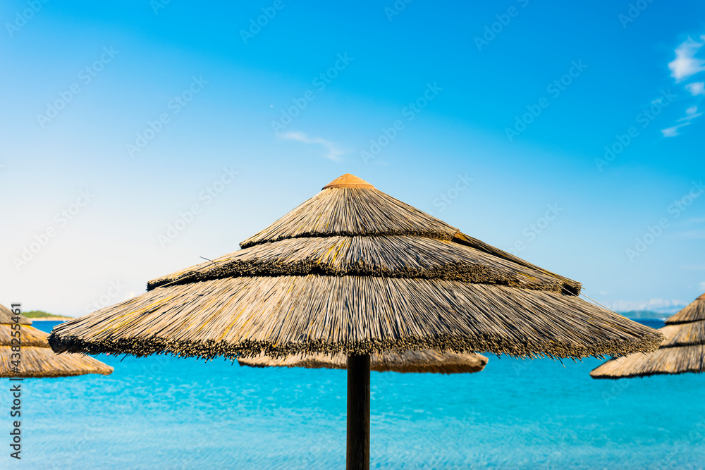 (Selective focus) Stunning view of a thatch umbrella in the foreground and beautiful turquoise sea in the background. Romazzino Beach, Porto Cervo, Sardinia, Italy. (Selective focus) Stunning view of a thatch umbrella in the foreground and beautiful turquoise sea in the background. Romazzino Beach, Porto Cervo, Sardinia, Italy.